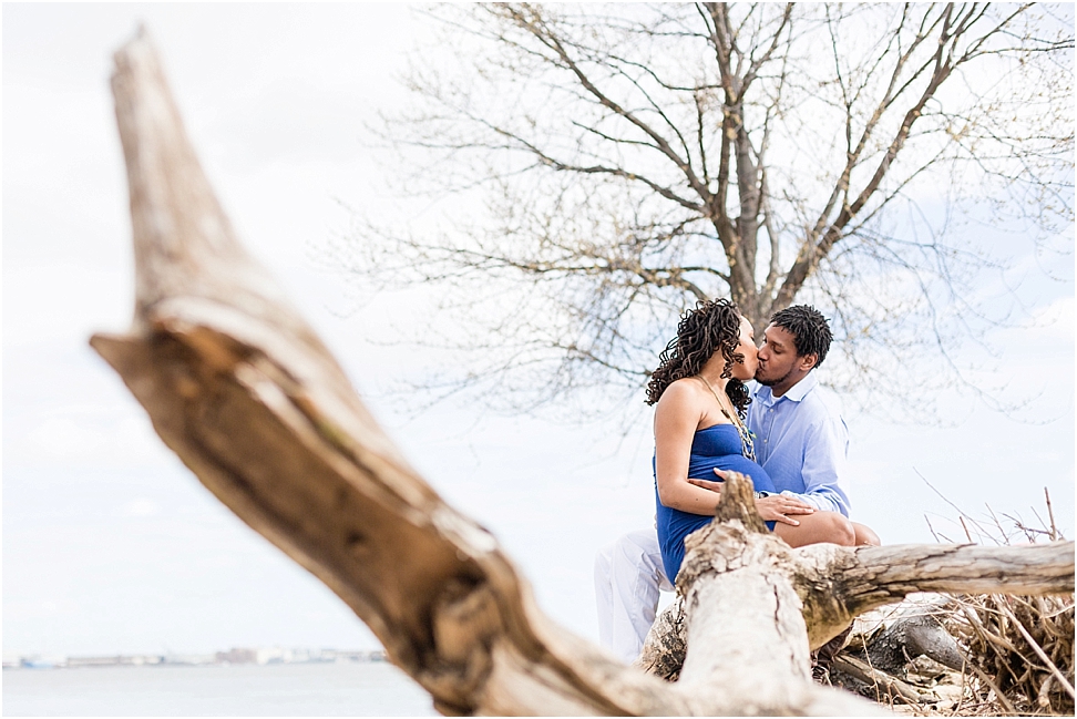 pregnant couple sitting on a piece of driftwood at river winds park