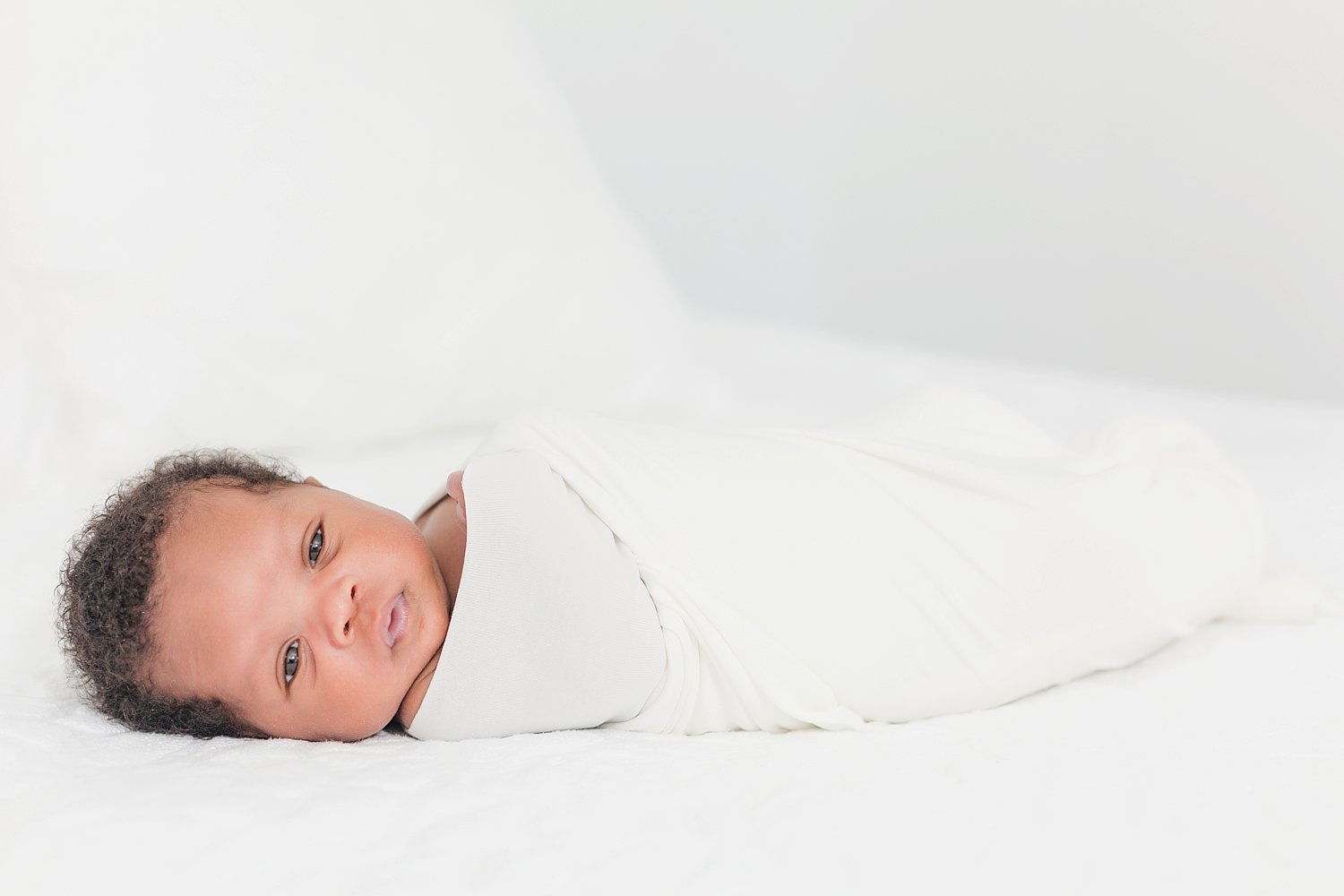 newborn baby boy in wrapped in white cloth for a minimalist newborn photo session in studio