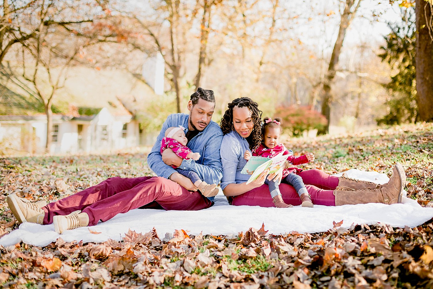 family of four sit on a neutral colored blanket to read a story book in the park