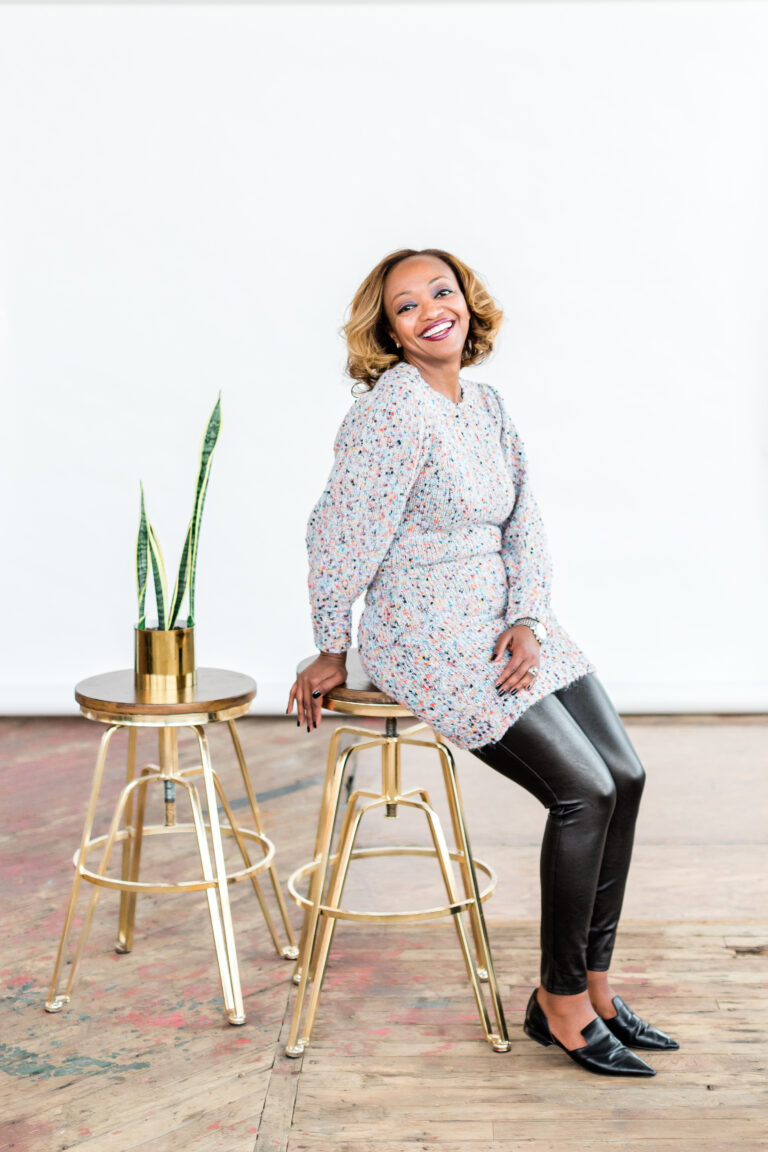 An entrepreneur sits on a stool smiling at the camera in front of a backdrop. Captured by Philadelphia personal branding photos photographer.